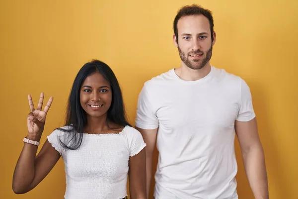 Interracial Couple Standing Yellow Background Showing Pointing Fingers Number Three — 图库照片