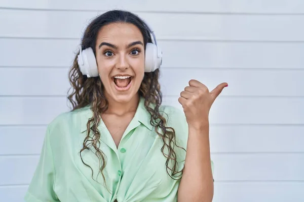 若いですヒスパニック系の女性は ヘッドフォンを使用して音楽を聞いて親指を指している側まで笑顔幸せなオープン口で — ストック写真