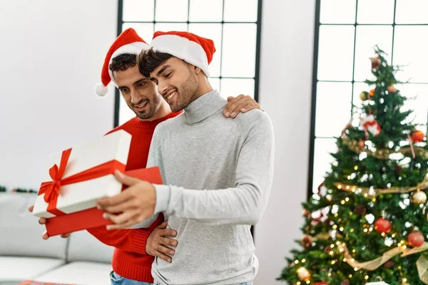 Dva Hispánští Muži Pár Překvapení Dárkem Stojící Vánočního Stromku Doma — Stock fotografie
