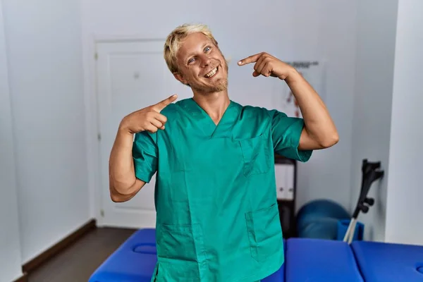 Young Blond Man Wearing Physiotherapist Uniform Standing Clinic Smiling Cheerful — Stockfoto