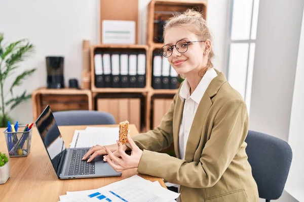Young Blonde Woman Business Worker Using Laptop Eating Cereal Bar — Stock Photo, Image