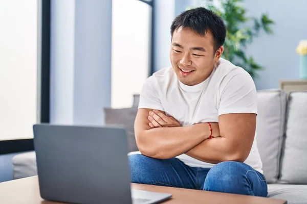 Young chinese man watching movie sitting on sofa at home