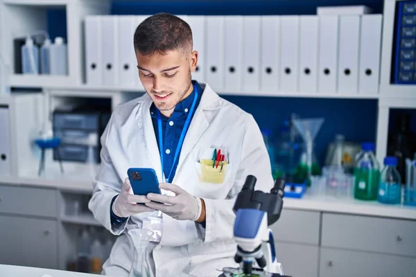 Young hispanic man scientist using smartphone at laboratory