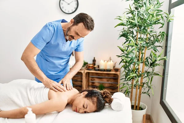 Middle age man and woman wearing therapist uniform having back massage session at beauty center