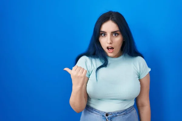 Young Modern Girl Blue Hair Standing Blue Background Surprised Pointing — Φωτογραφία Αρχείου