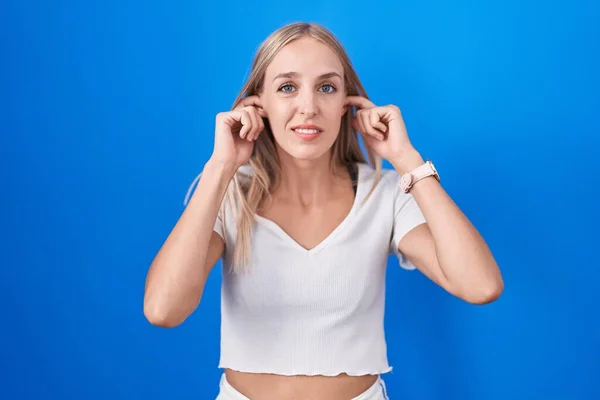 Mulher Caucasiana Jovem Sobre Fundo Azul Cobrindo Orelhas Com Dedos — Fotografia de Stock