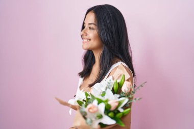 Brunette woman holding bouquet of white flowers looking to side, relax profile pose with natural face and confident smile. 