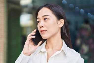 Young chinese woman talking on smartphone with serious expression at street