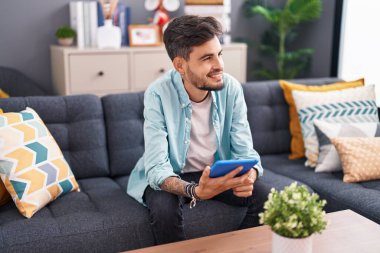 Genç İspanyol adam evdeki koltukta otururken dokunmatik ped kullanıyor.