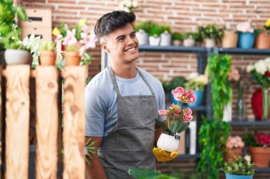 Çiçekçide çiçekleri tutarken gülümseyen İspanyol genç adam.