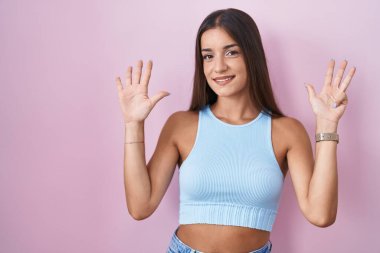 Pembe arka planda duran genç esmer kadın dokuz numarayı gösterip işaret ederken kendinden emin ve mutlu bir şekilde gülümsüyor.. 