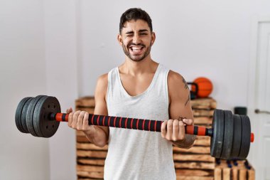 Genç İspanyol adam antrenmanında. Ağırlığını koyup kameraya seksi bir ifadeyle bakıyor. Neşeli ve mutlu bir yüz.. 
