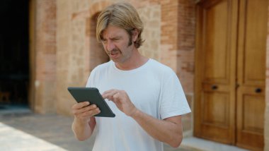 Sarışın genç adam sokakta ciddi bir ifadeyle dokunmatik ped kullanıyor.