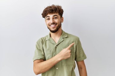 Young arab doctor man standing over isolated background cheerful with a smile on face pointing with hand and finger up to the side with happy and natural expression 