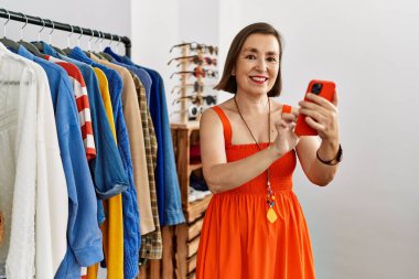 Orta yaşlı İspanyol kadın perakende dükkanında akıllı telefon kullanarak gülümsüyor.