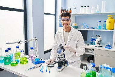 Laboratuvarda mikroskop kullanarak bilim adamı üniforması giyen genç bir İspanyol.