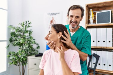 Orta yaşlı erkek ve kadın sırıtarak boyun gererek fizyoterapi kliniğinde rehabilitasyon seansı yapıyorlar.