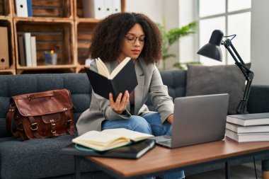 Young african american woman psychologist using laptop and reading book at psychology center