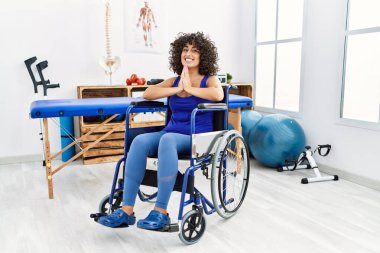 Tekerlekli sandalyede oturan genç orta doğulu bir kadın. Birlikte dua edip af diliyor. Kendinden emin bir şekilde gülümsüyor.. 