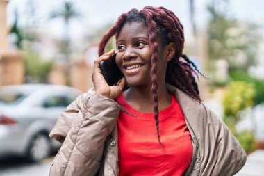 Afro-Amerikalı kadın gülümsüyor. Akıllı telefondan konuşuyor.