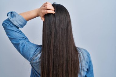 İspanyol kadın mavi arka planda geriye doğru duruyor. Elleri kafasında şüpheyi düşünüyor. 