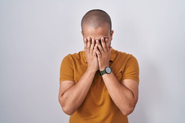 Hispanic man with beard standing over white background with sad expression covering face with hands while crying. depression concept. 