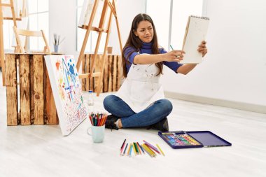 Resim stüdyosunda şüpheli bakışlı genç Latin kadın defter çizimi yapıyor.