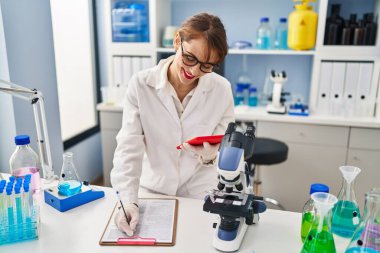 Laboratuvarda çalışan dokunmatik ped kullanan, bilim adamı üniforması giyen beyaz bir kadın.
