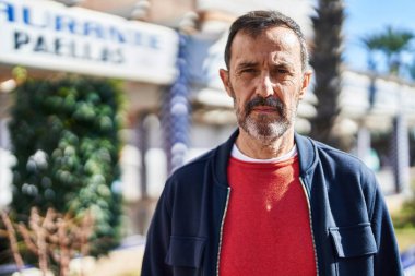 Orta yaşlı, rahat yüzlü bir adam sokakta dikiliyor.