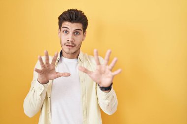 Sarı arka planda duran İspanyol genç adam korku ifadesinden korkmuş ve dehşete düşmüş. El hareketlerini durdur, şok içinde bağır. panik konsepti. 