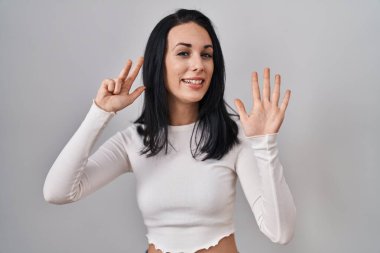 Hispanic woman standing over isolated background showing and pointing up with fingers number eight while smiling confident and happy. 