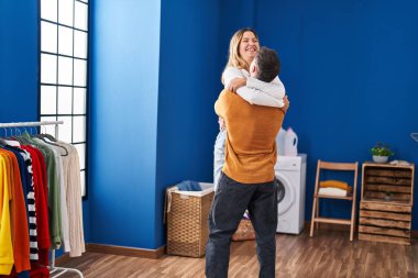 Genç adam ve kadın sırıtan bir çift çamaşırhanede birbirlerine sarılıyorlar.