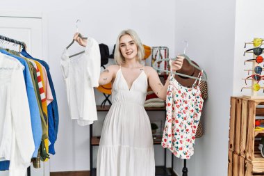 Giysi dükkanında kendine güvenen beyaz bir kadın gülümsüyor.