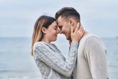 Kadın ve erkek gülümsüyor. Kendilerine güveniyorlar. Deniz kenarında sarılıyorlar.