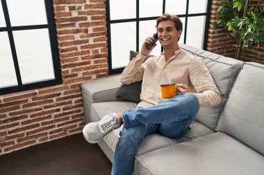 Kafkasyalı genç adam akıllı telefondan konuşuyor evde kahve içiyor.