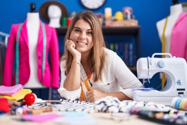 Young woman tailor smiling confident sitting on table at sewing studio