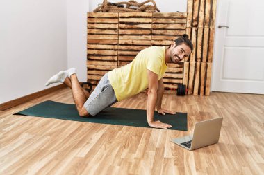 Handsome hispanic man training looking at video tutorial on laptop at the gym