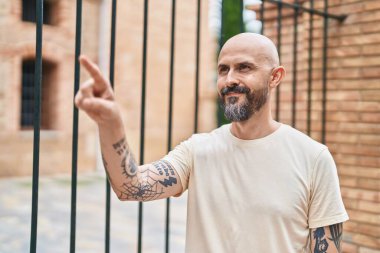 Genç kel adam gülümsüyor. Kendine güveni tam, parmağıyla sokağı gösteriyor.