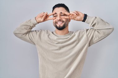 Soyutlanmış arka planda duran yakışıklı genç adam barış sembolü yapıyor. Yüzünde parmaklar, gülümseyerek zaferi gösteriyor. 