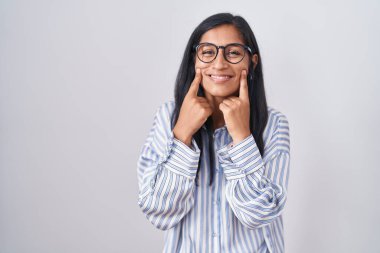 Young hispanic woman wearing glasses smiling with open mouth, fingers pointing and forcing cheerful smile 