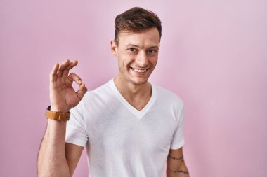 Caucasian man standing over pink background smiling positive doing ok sign with hand and fingers. successful expression. 