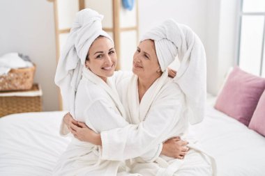 Mother and daughter wearing bathrobe hugging each other at bedroom