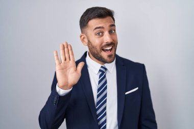 Yakışıklı İspanyol takım elbiseli ve kravatlı adam merhaba diyor mutlu ve gülümseyen, dostça bir hoş geldin jesti. 