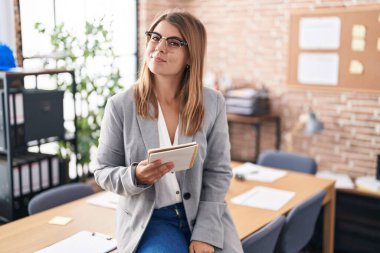 Ofiste çalışan genç İspanyol kadın. Gözlüklü, gülümseyen, yan bakan ve düşünen.. 
