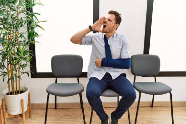 Yakışıklı genç adam, doktor bekleme odasında kolundan yaralanmış, bağırıyor ve ağızdan ağıza bağırıyor. iletişim konsepti. 