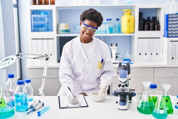 アフリカ系アメリカ人女性科学者の制服を着た女性研究室で作業クリップボードに書き込みます — ストック写真