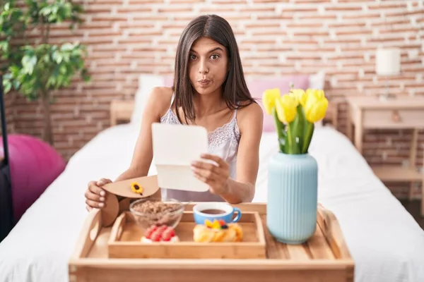 Brunette Young Woman Eating Breakfast Bed Reading Letter Puffing Cheeks — Stockfoto