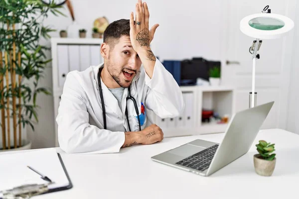 Young doctor working at the clinic using computer laptop surprised with hand on head for mistake, remember error. forgot, bad memory concept.