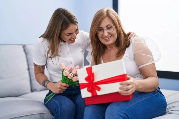 Mother and daughter surprise with gift and flowers hugging each other at home