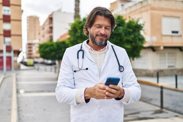 中年男性医師笑顔自信を持って使用してスマートフォンでストリート — ストック写真